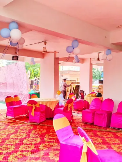 A view of the seating arrangement for a Kuan Pujan celebration. The space is decorated with balloon clusters on the ceiling and pillars, with bright pink chair covers adding to the festive look.