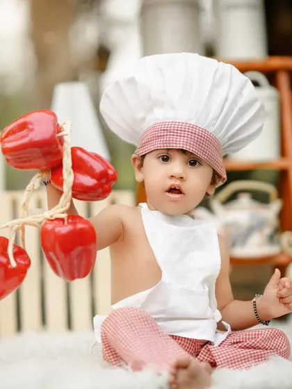 A proud little chef showing off his fresh red peppers. The bright colors and his curious expression make this a wonderful and vibrant portrait.