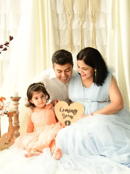 A family maternity session in our bright, boho-themed studio. The older daughter holds a "Coming Soon" sign, making this a joyful and inclusive way to announce a new addition to the family.