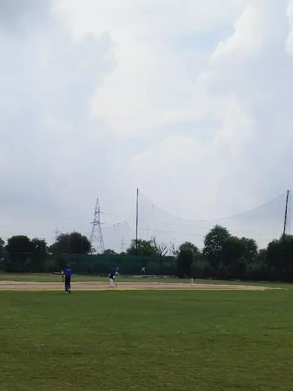 A wide shot of a match in progress during the PS Cup U-17 tournament. The ground is large enough to host competitive matches with proper fielding positions.
