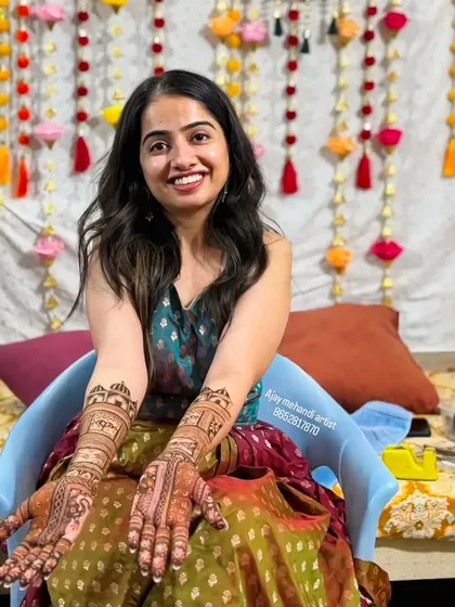 A happy client sitting in front of a festive backdrop, showing her full-arm mehndi.