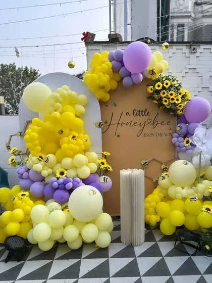 A sweet "A Little Honeybee is on the Way" themed baby shower. This outdoor setup uses yellow and purple balloons to create honeycomb and bee shapes, with sunflower accents adding to the charm.