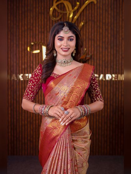 A model in a beige and red silk saree. This is a classic combination, and the drape is styled to look elegant and sophisticated for a reception or formal event.