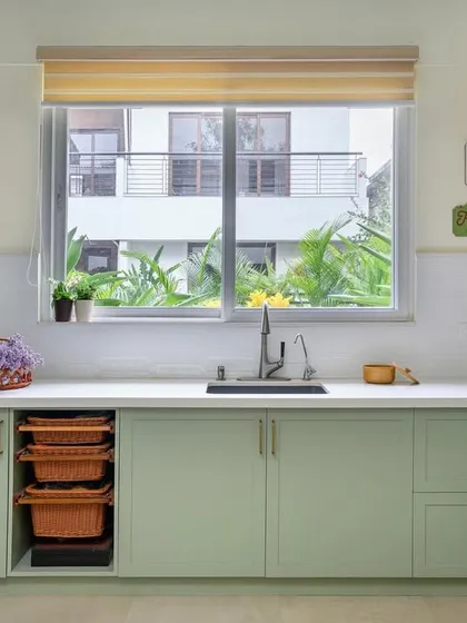 Another view of the 'House of Kismish' kitchen, highlighting the sage green cabinets, white subway tile backsplash, and a large window over the sink that overlooks the garden.