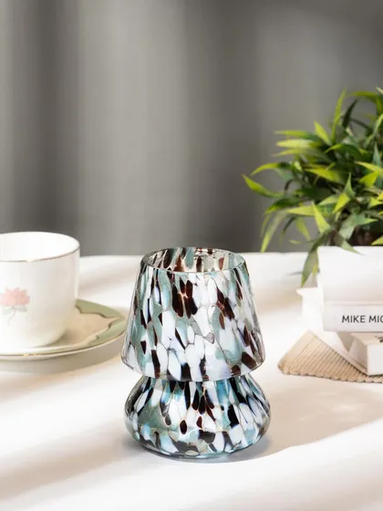 A home decor shot of a blue-toned mushroom candle holder. The styling with a teacup and books suggests a relaxing moment of reading and enjoying the ambiance.