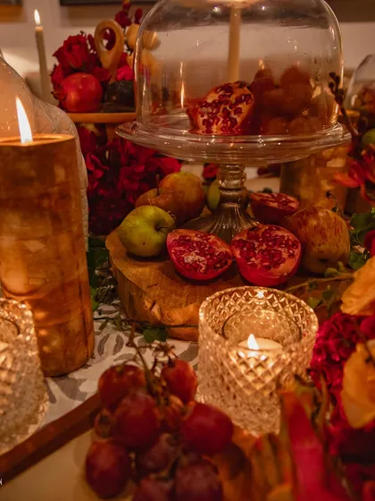 A close-up on a section of the table, highlighting the textures of cut pomegranates, grapes, and cut-glass candle holders. Every detail is carefully chosen to contribute to the overall sensory experience of the event.