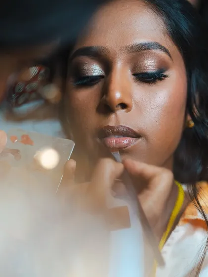 A candid, artistic shot of Anukraha's reception makeup application. The focus is on creating that flawless, glowing base and a perfect nude lip.