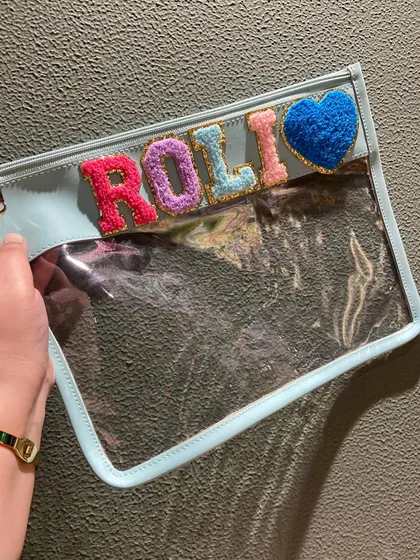 Our clear travel pouch in a cool blue, personalised for 'Roli' with a cute heart patch. Let your essentials shine through in style.