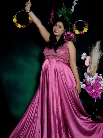 A joyful and celebratory solo portrait in the studio. The mom-to-be's happy expression and pose, combined with the elegant pink gown, create a truly radiant image.