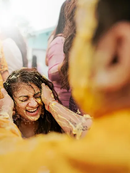 A close-up of the bride laughing as Haldi is applied to her. This candid shot captures a moment of pure, unscripted joy.