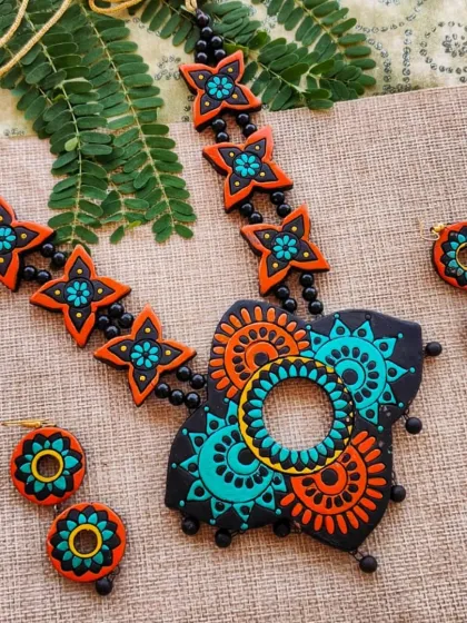 This unique necklace features a butterfly-shaped pendant with a mandala design inside. The black, orange, and sea-green color combination is modern and striking.