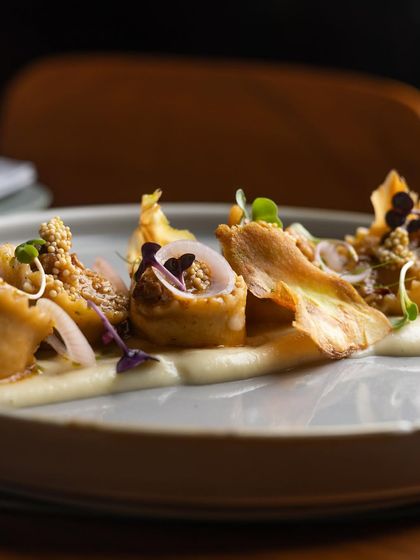 The elegant plating of our corn and ricotta tortellini, showing the delicate arrangement of the pasta, parsnip crisps, and pickled mustard seeds.