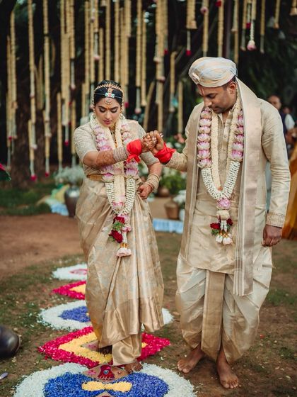 A bride and groom during their wedding rituals. Their matching cream and gold outfits, including his silk dhoti and her Kanchipuram saree, were designed to reflect South Indian wedding traditions.