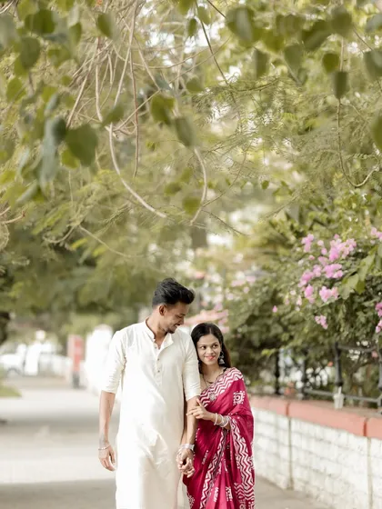 A candid walking shot of the couple holding hands and sharing a smile, framed by lush greenery. This captures the easy and natural chemistry between them.