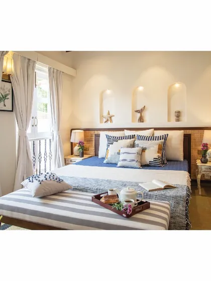 This bedroom in our Goa villa is styled with a coastal theme. The mood board included tropical motifs, reflected in the blue and white bedding, starfish decor in the wall niches, and light, airy curtains. It's a bright and cheerful space designed for a holiday mindset.