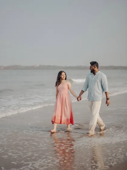 The couple walking through the shallow waves, with their reflection visible in the water. This is a classic pre-wedding beach photo that feels both timeless and spontaneous.