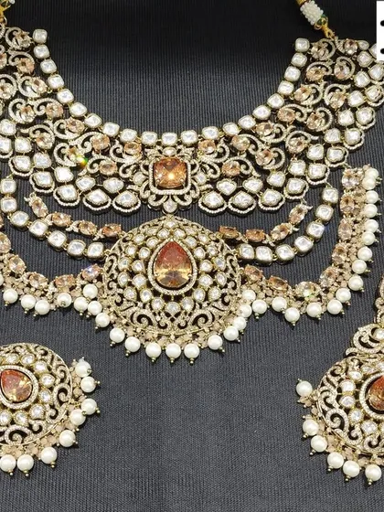 A close-up of a multi-layered Polki necklace set with champagne-colored stones and pearl drops. This set, which includes a choker, earrings, and maang tikka, is available for both rent and purchase.