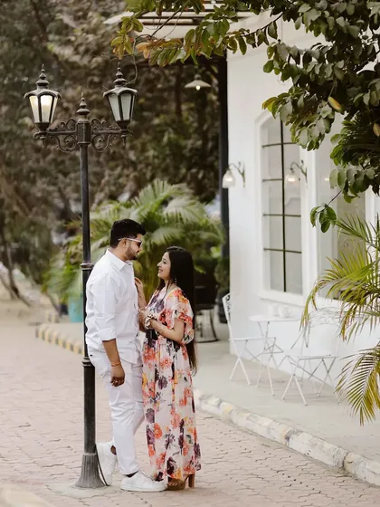 A lovely outdoor portrait of a couple standing by a vintage lamppost. The white building and greenery in the background provide a clean and classic European street vibe.