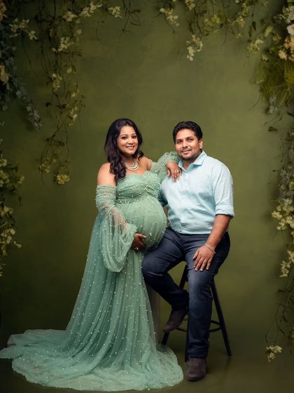 A lovely couple's portrait against a floral green backdrop. The mom-to-be is radiant in her off-shoulder green tulle gown.