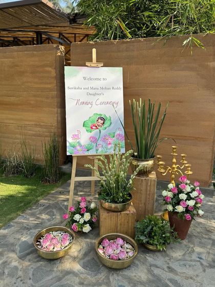 The welcome sign for Tridha's naming ceremony, featuring a custom watercolor illustration and surrounded by lotus flowers.