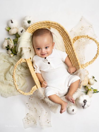 A serene and beautiful overhead shot of a baby boy in a wicker basket. The neutral tones and soft textures create a peaceful and classic newborn-style portrait.
