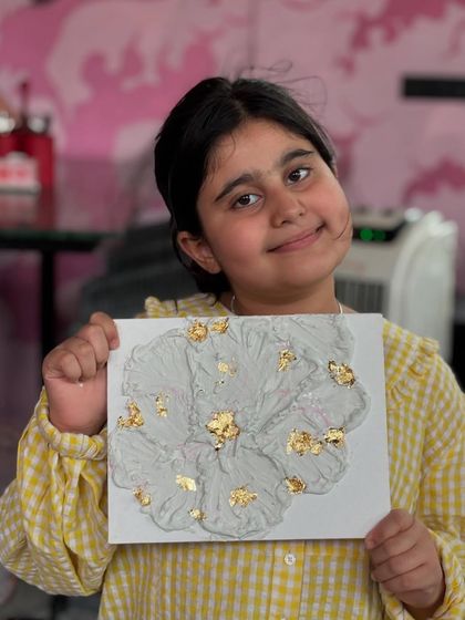 A young artist beaming with pride as she holds her textured flower with gold foil accents. Art is for everyone, at any age.