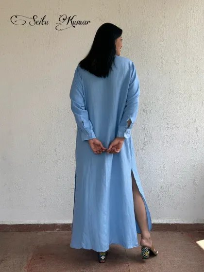 The back view of the long blue shirt dress, highlighting the side slits that add movement and a touch of allure.