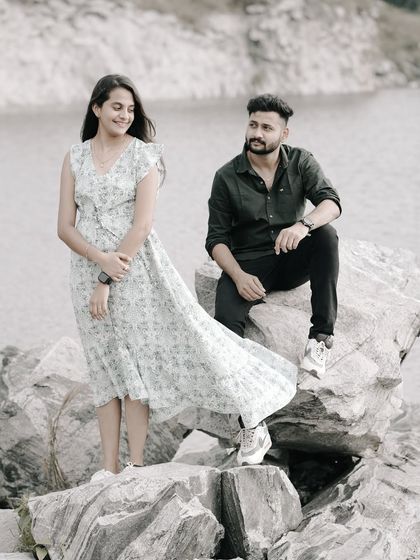 A relaxed and happy shot of a couple on rocks by a lake, the wind catching the bride's dress.