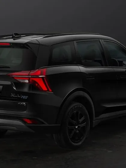 A three-quarter rear view of the all-black Mahindra XUV700, highlighting its taillights and muscular stance in a controlled studio environment.