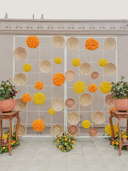 A creative and rustic photo backdrop made from marigolds and woven baskets, adding a unique and textural element to the Haldi decor.