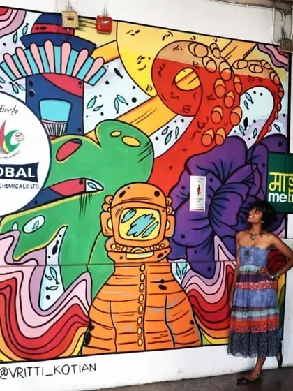 An artist poses with her vibrant mural inside a Mumbai Metro station. The artwork features an astronaut, an octopus, and a lighthouse, bringing a splash of color and imagination to the daily commute.