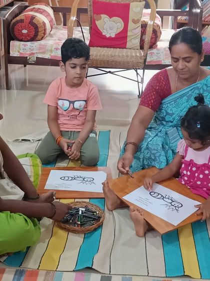 An adult helps a young child with a coloring sheet of an ant, making the activity accessible for all ages.