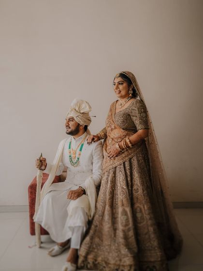 A regal, full-length portrait. The groom is seated holding a ceremonial sword, while the bride stands by his side, creating a powerful and traditional image.