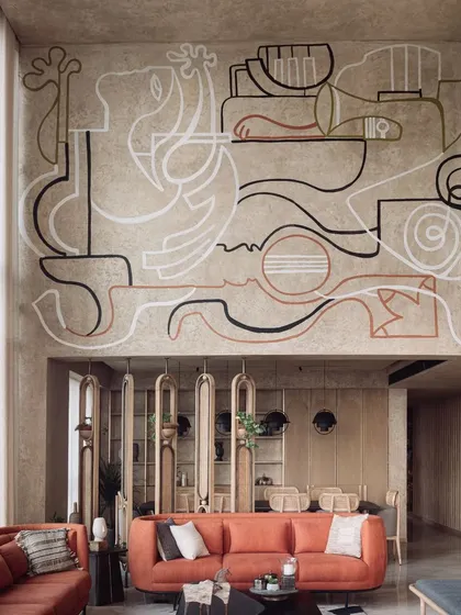 A double-height living room featuring a minimalist line-art mural that spans the entire wall. The artwork adds a layer of sophistication and storytelling without overwhelming the serene, earthy interior design.