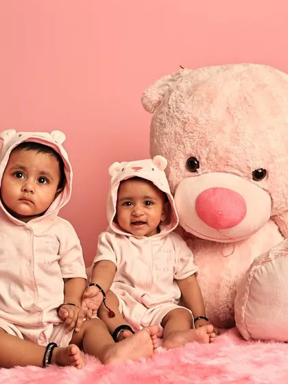 Two sweet babies in matching bear-hooded rompers pose with a giant teddy bear. This setup is perfect for a cozy and adorable twin or sibling photoshoot.
