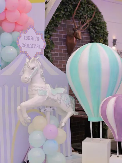 A delightful corner of a pastel carnival setup, featuring a carousel horse and hot air balloon props. The soft mint, purple, and pink colors create a dreamy and gentle atmosphere perfect for a first birthday.