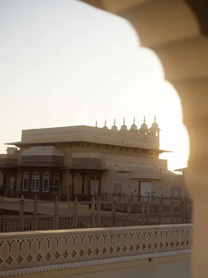 A view of the Chomu Palace at sunset, framed by an archway. This shot captures the romantic, golden-hour light that makes palace weddings in Rajasthan so magical.