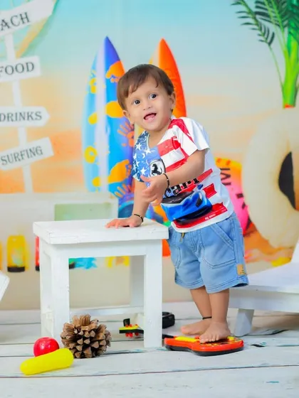 A toddler in a patriotic outfit stands in our beach setup, ready to play. The surfboards and beach signs create a perfect summer vibe.