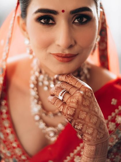 A confident and direct bridal portrait. The focus is on her expressive eyes and the intricate details of her mehndi and wedding ring.