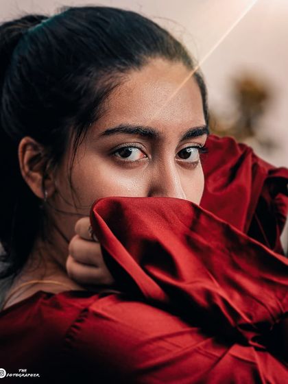 An intense and emotive close-up portrait. The way the model uses her sleeve to frame her face creates a sense of mystery and intimacy.