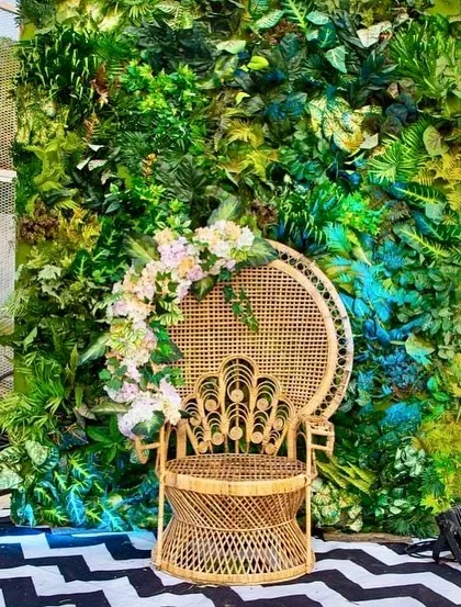 A beautiful peacock chair set against a lush green wall for a photo booth. We can source or fabricate unique furniture pieces to match your event's theme.