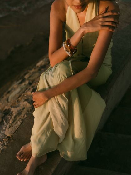 A quiet, contemplative portrait of the bride sitting by the sea in Muscat. The warm, golden hour light beautifully illuminates her, creating a soft and elegant mood.