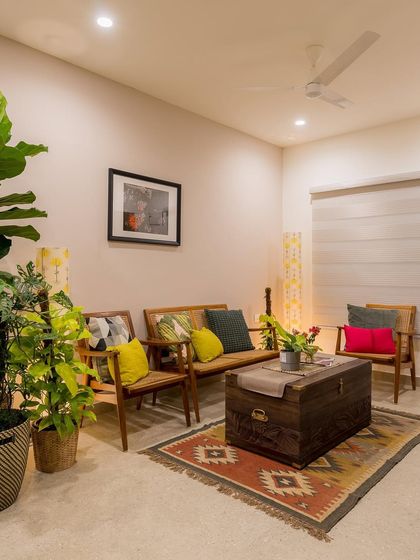 This living room is a cozy and inviting space, furnished with classic wooden pieces and a plush rug. The addition of tropical plants and colorful cushions brings life and personality to the neutral palette.