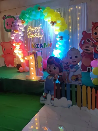 A clear view of the Cocomelon stage setup with the lit-up balloon arch and character props. The lighting adds a magical touch to the entire decoration.