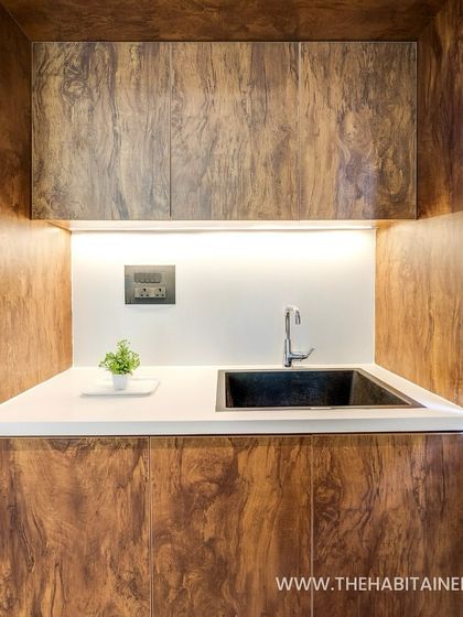 A compact and stylish kitchenette with wood-grain cabinets and under-cabinet lighting, perfect for a guest pod or studio.