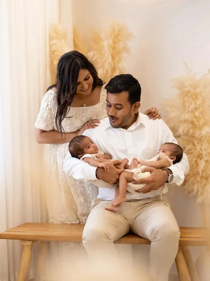 A proud father holds his two newborn babies, with his wife looking on with love. Capturing the family connection is a key part of my newborn twin photography sessions.