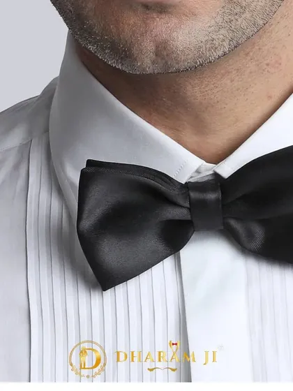 A close-up of a classic black satin bow tie on a pleated tuxedo shirt. This is the timeless finishing touch for any black-tie outfit.