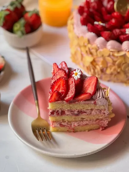 A slice of our Fresh Cream Strawberry Cake, served on a pretty pink and white striped plate. This image captures a perfect moment of indulgence, ready to be enjoyed.