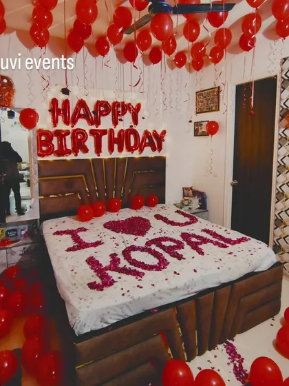 I can turn any bedroom into a romantic surprise. This setup includes red balloons on the ceiling, 'Happy Birthday' foil letters, and a personal message on the bed made from rose petals.