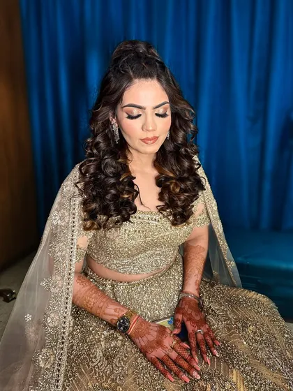 A full view of this sangeet bride's look. The combination of a braided half-updo, tight curls, and shimmering makeup creates a youthful and festive style.